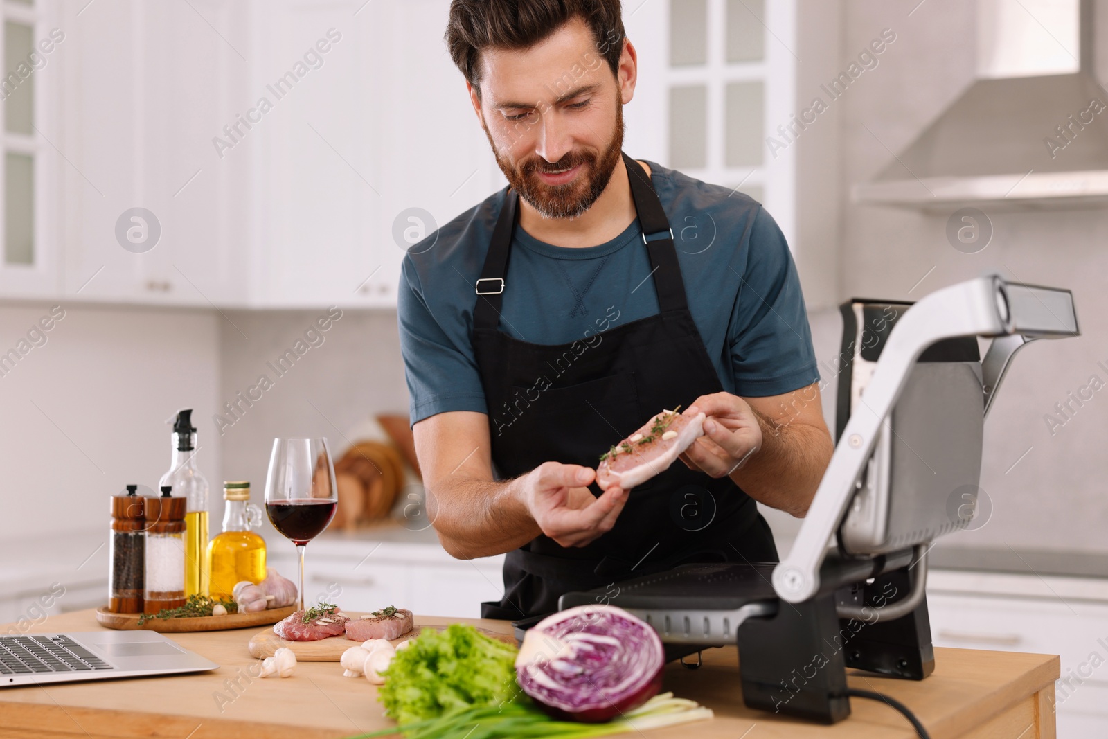 Photo of Man making dinner while watching online cooking course via laptop in kitchen