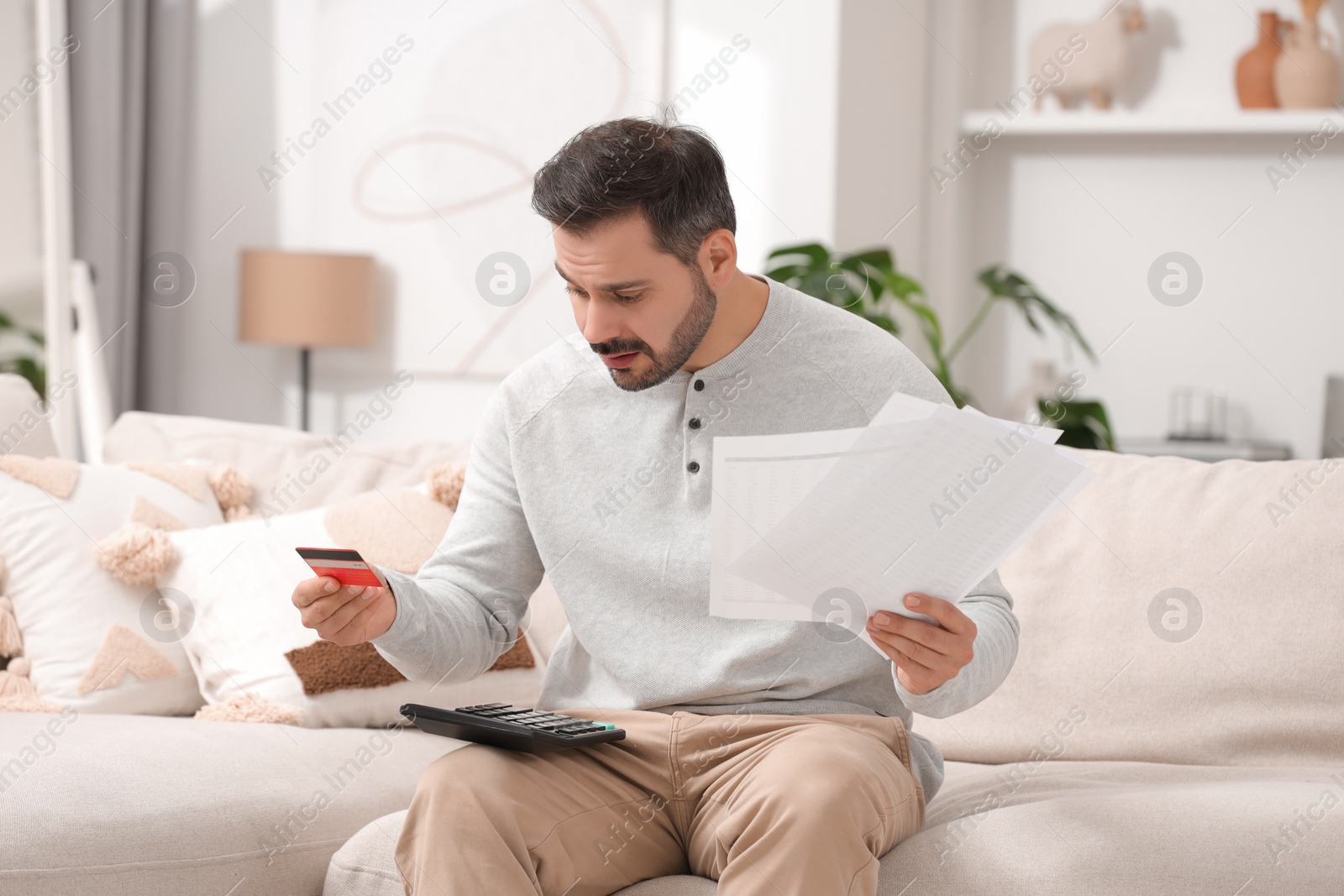 Photo of Confused man with debt notifications, calculator and credit card planning budget at home. Financial problem