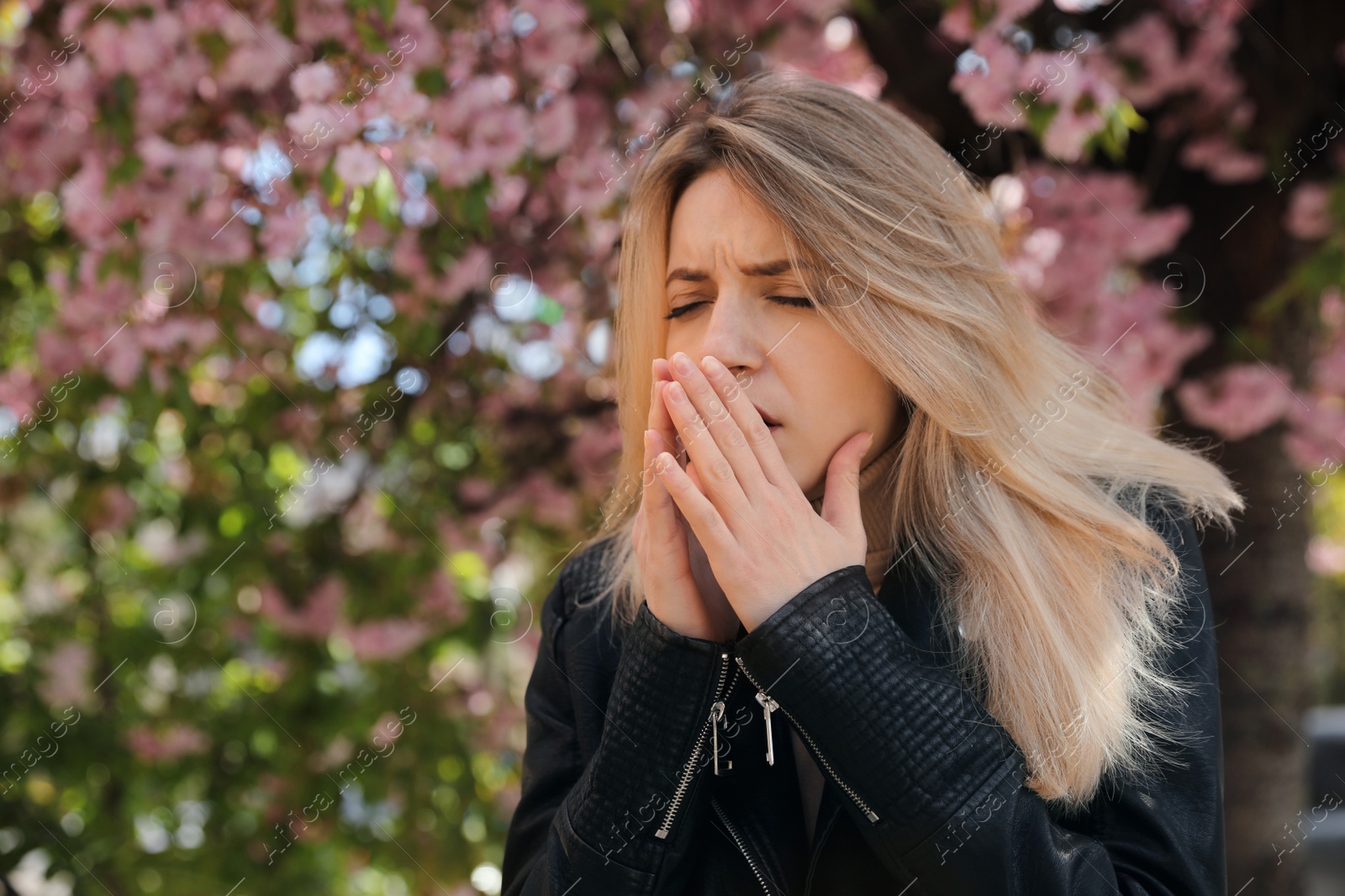 Photo of Woman suffering from seasonal pollen allergy near blossoming tree outdoors