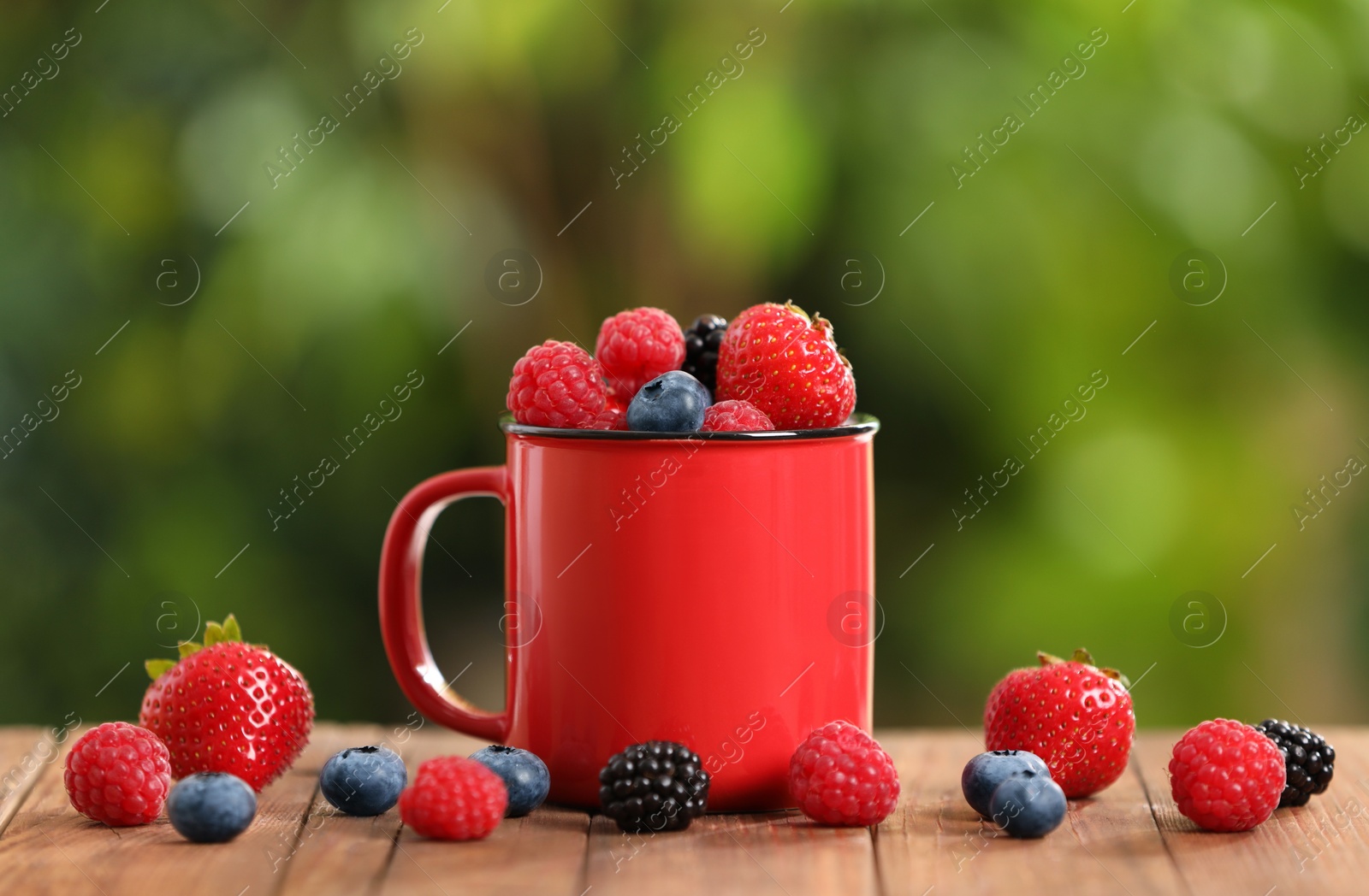 Photo of Mug with different fresh ripe berries on wooden table outdoors