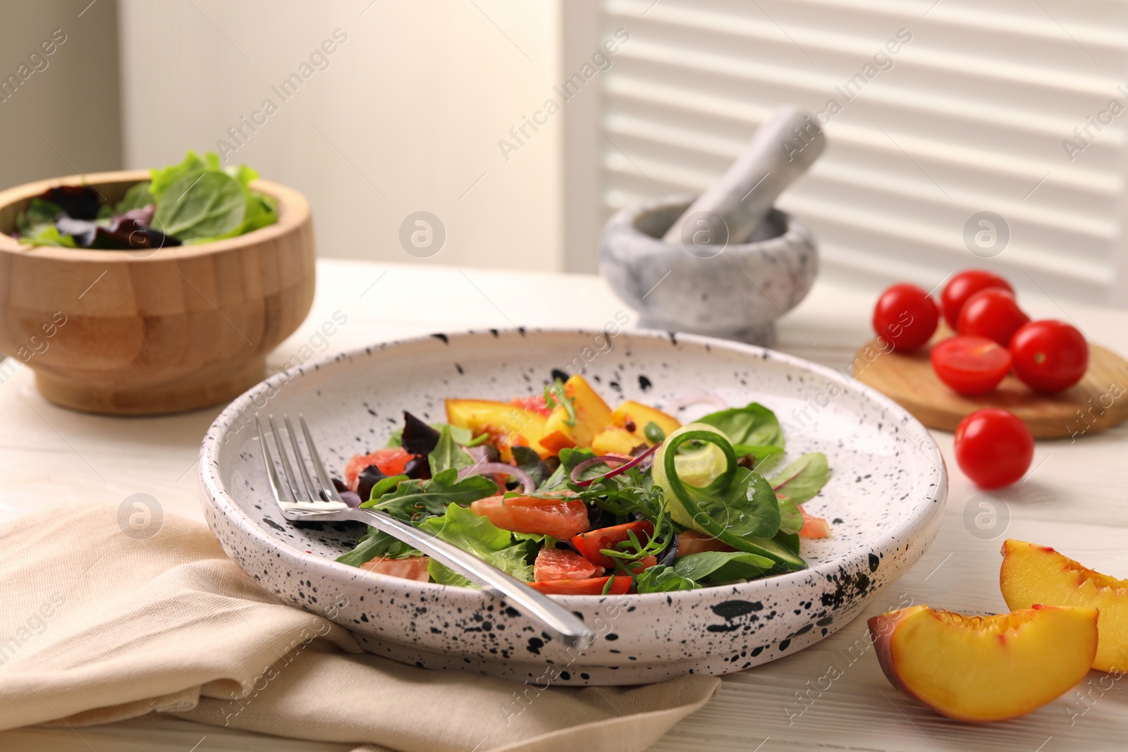 Photo of Delicious salad with vegetables and peach served on white wooden table