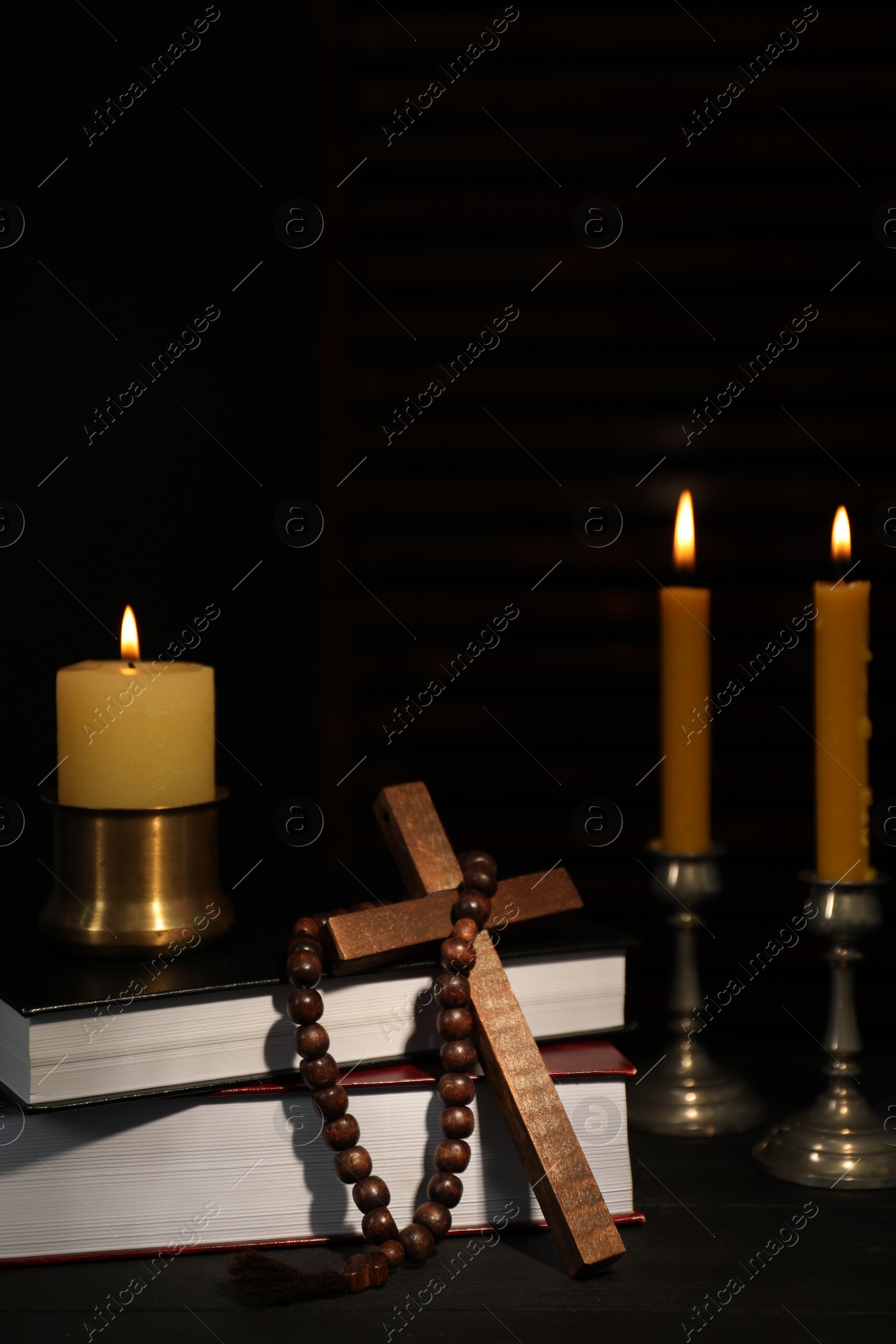 Photo of Church candles, Bible, rosary beads and cross on table in darkness