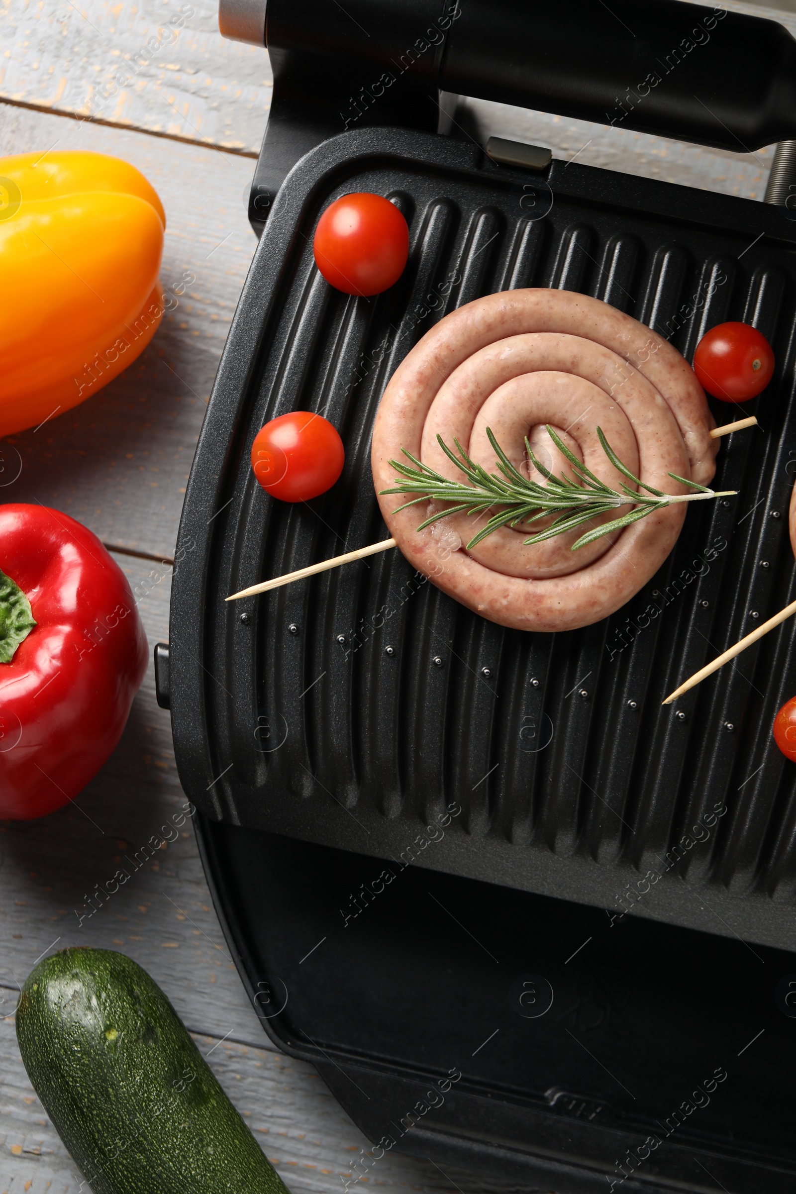 Photo of Electric grill with homemade sausages, rosemary and vegetables on rustic wooden table, flat lay