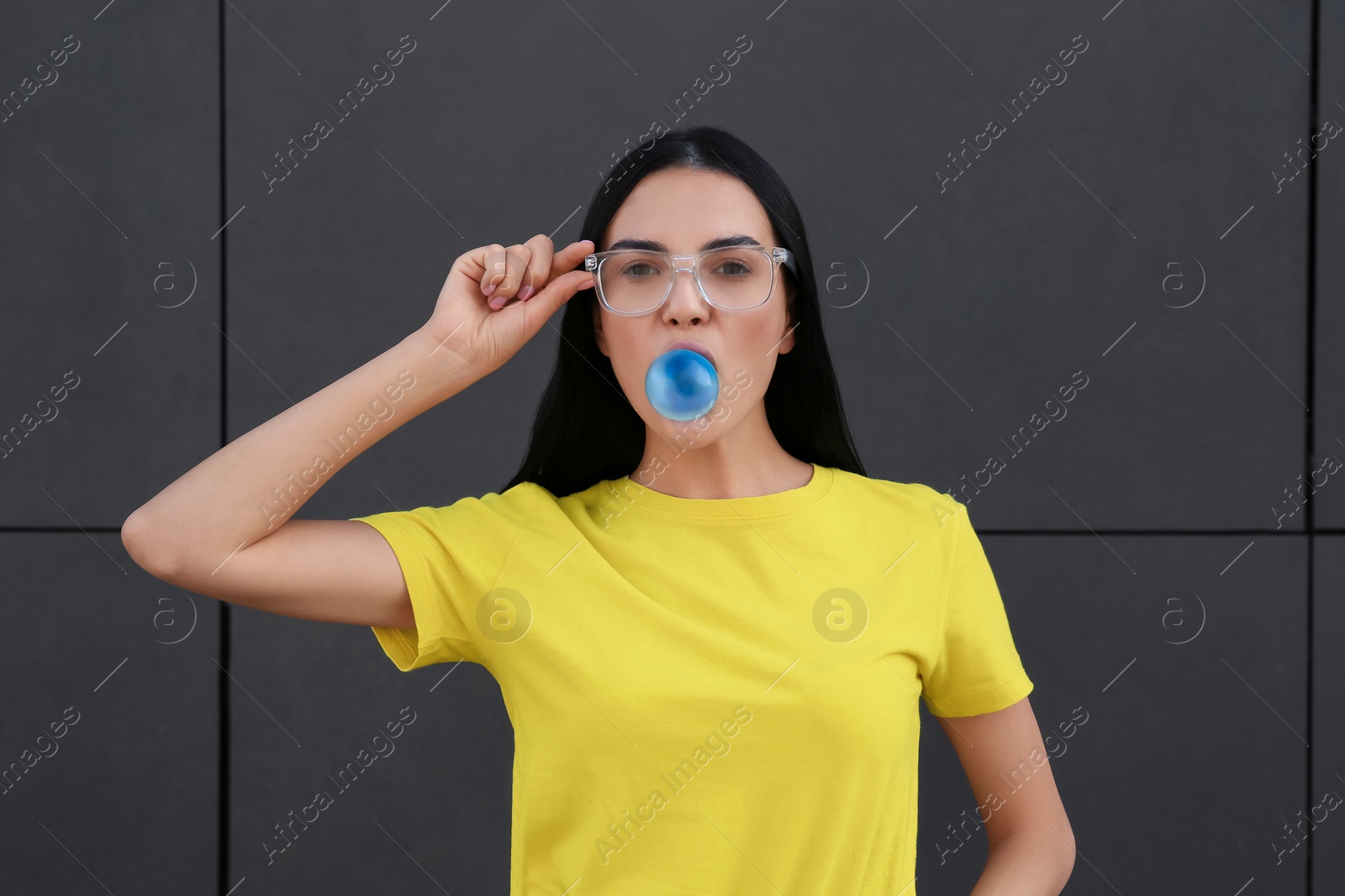 Photo of Beautiful woman blowing gum near dark tiled wall outdoors