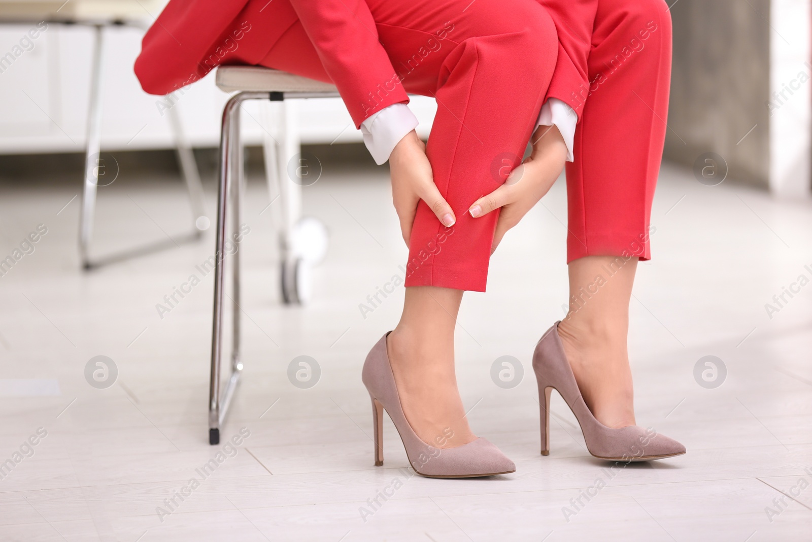 Photo of Young woman suffering from leg pain in office