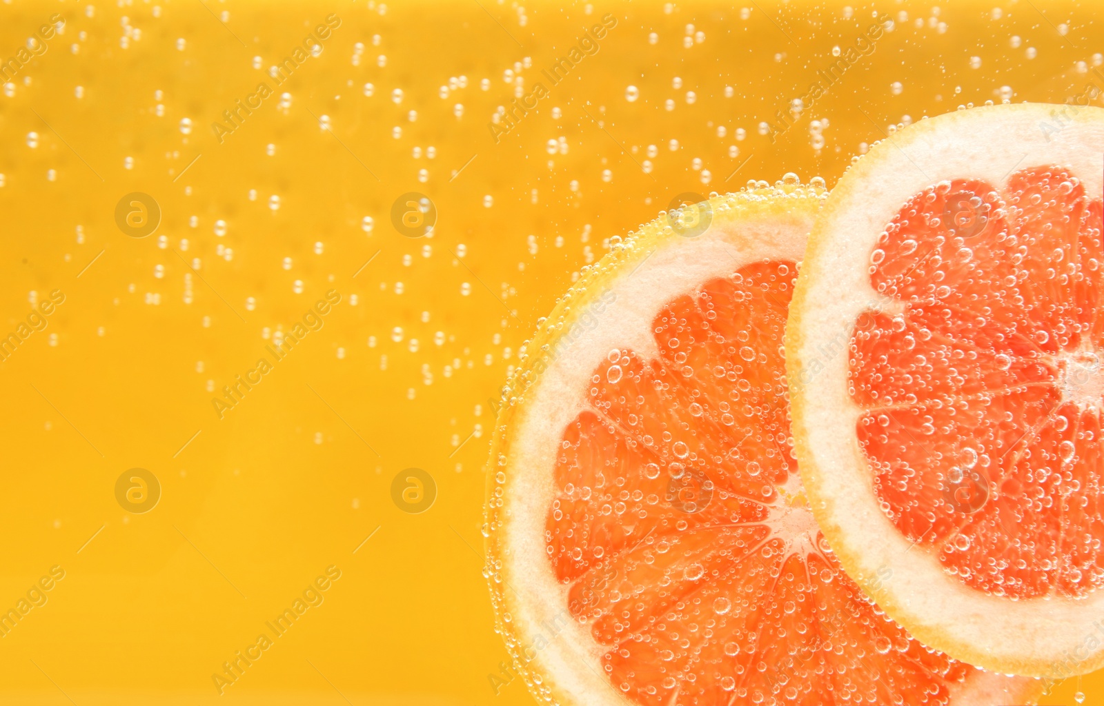 Photo of Slice of grapefruit in sparkling water on yellow background, closeup with space for text. Citrus soda