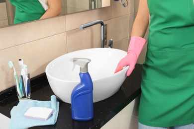 Photo of Woman cleaning sink with rag in bathroom