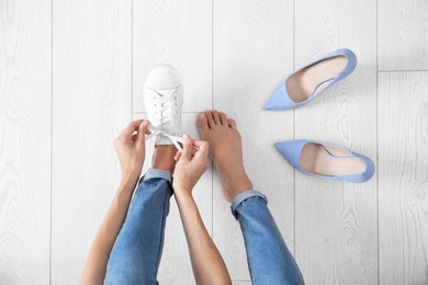 Young woman changing shoes on wooden background, top view