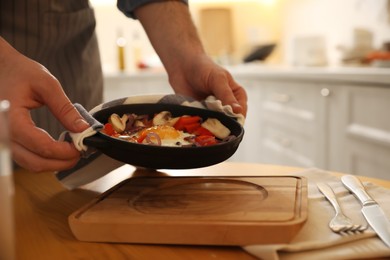 Photo of Man putting frying pan with fresh egg and vegetables on wooden board, closeup