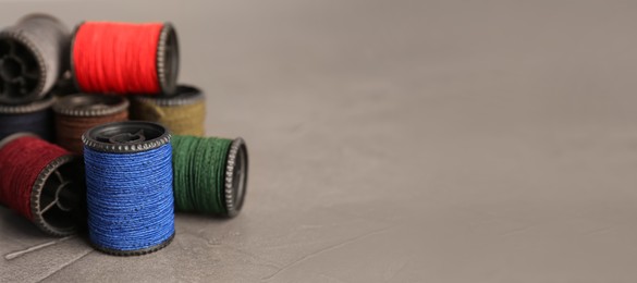 Set of color sewing threads on grey table, closeup. Space for text