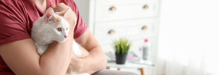 Young man with cute cat at home, space for text. Banner design