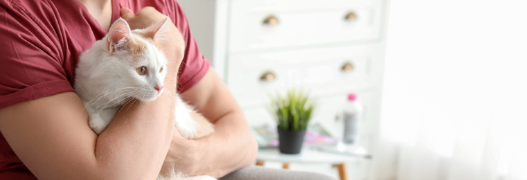 Image of Young man with cute cat at home, space for text. Banner design