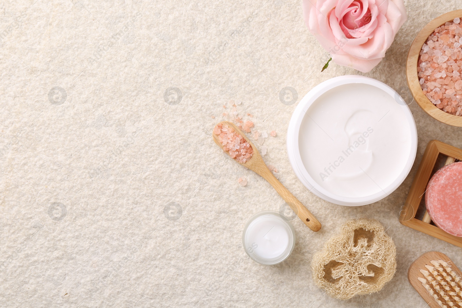 Photo of Flat lay composition with moisturizing cream in open jar and other body care products on light textured table. Space for text