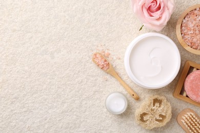 Flat lay composition with moisturizing cream in open jar and other body care products on light textured table. Space for text