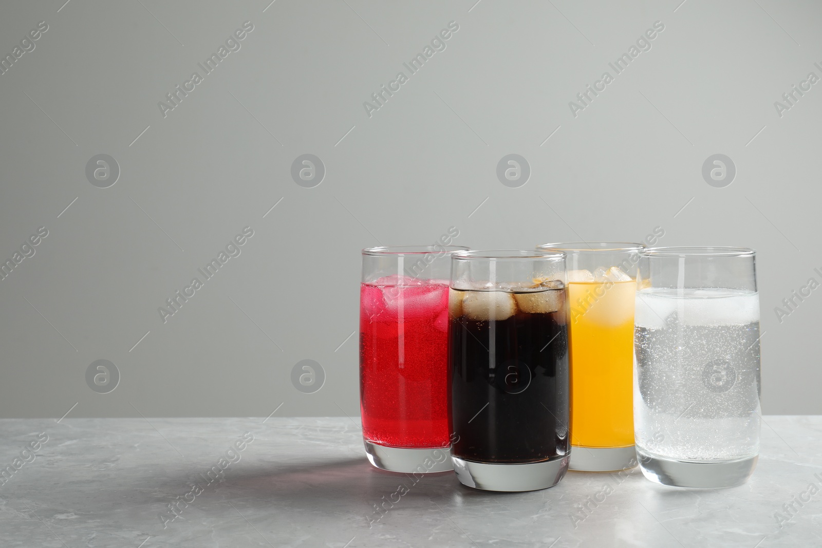 Photo of Glasses of different refreshing soda water with ice cubes on light grey marble table. Space for text