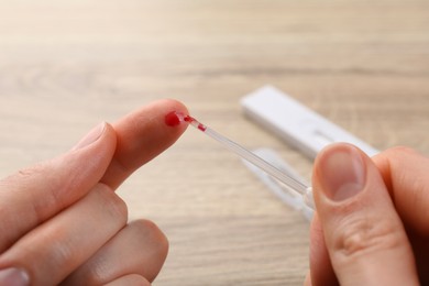 Photo of Laboratory testing. Woman taking blood sample from finger with pipette at table, closeup