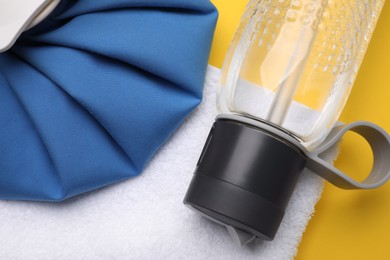 Photo of Bottle of water, cold compress and towel on yellow background, flat lay. Heat stroke treatment
