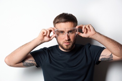 Young working man in protective glasses on light background