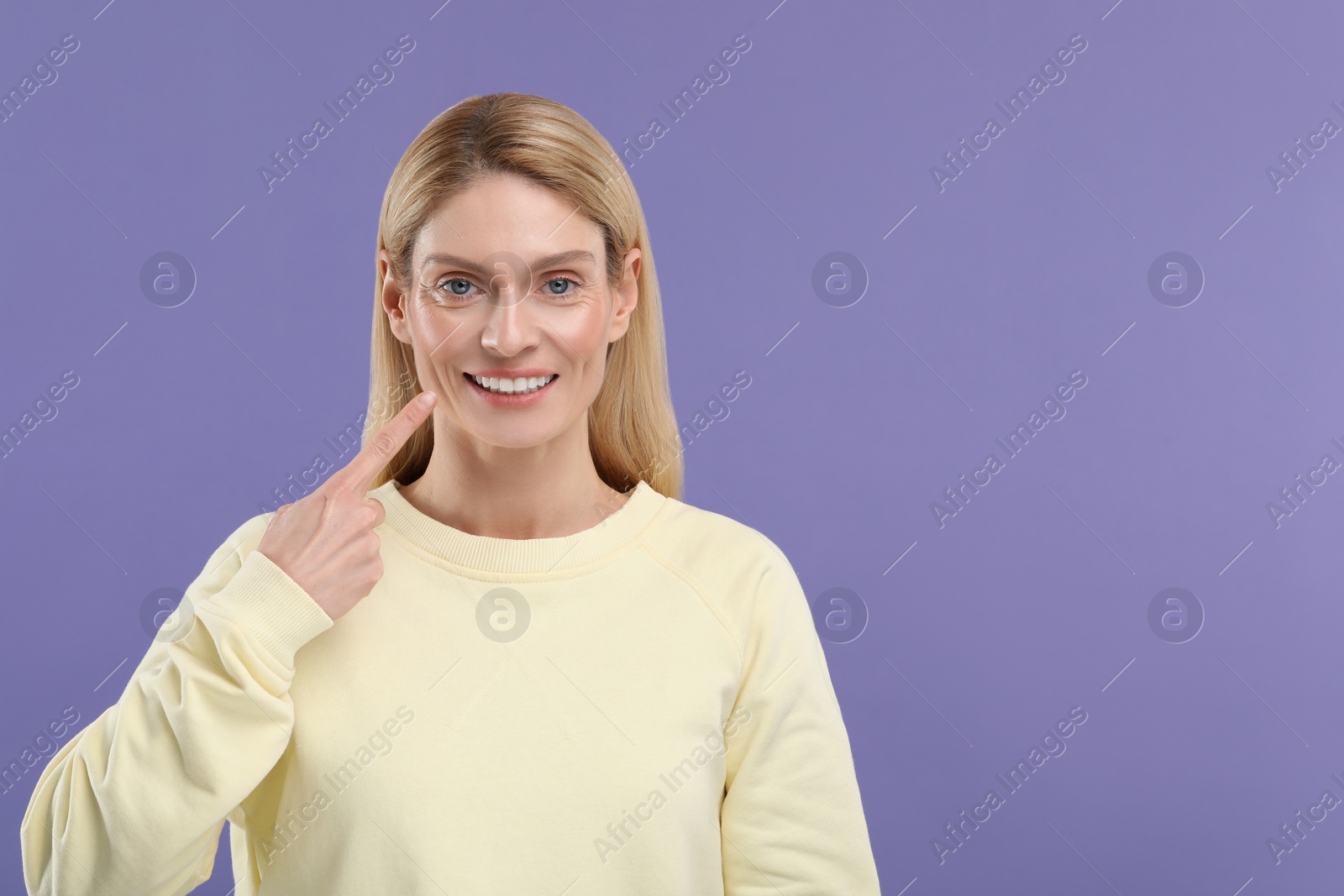 Photo of Woman showing her clean teeth and smiling on violet background, space for text