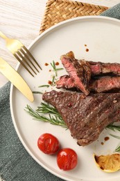 Photo of Delicious grilled beef steak, tomatoes, spices and cutlery on light wooden table, top view