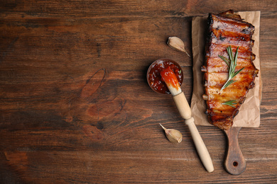 Photo of Tasty grilled ribs with sauce on wooden table, flat lay. Space for text