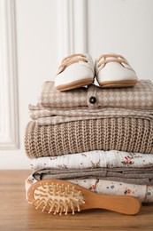 Photo of Baby clothes, shoes and hairbrush on wooden table