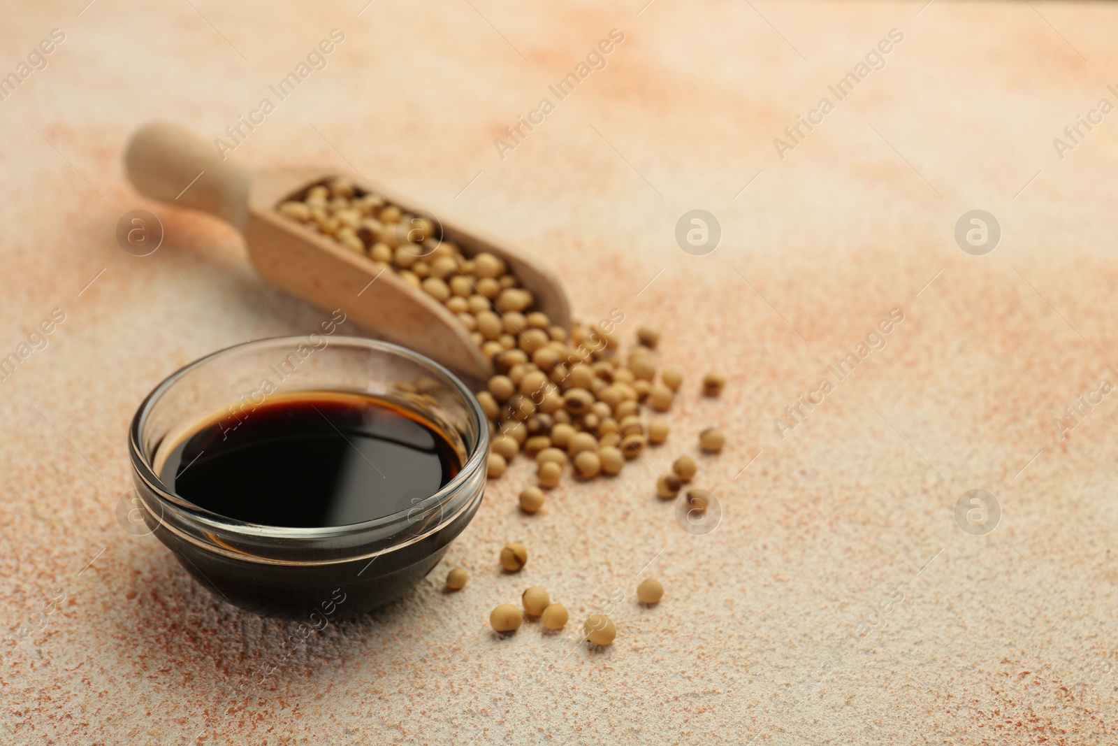 Photo of Soy sauce in bowl and beans on beige textured table, closeup. Space for text