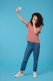 Photo of Emotional young woman taking selfie on light blue background