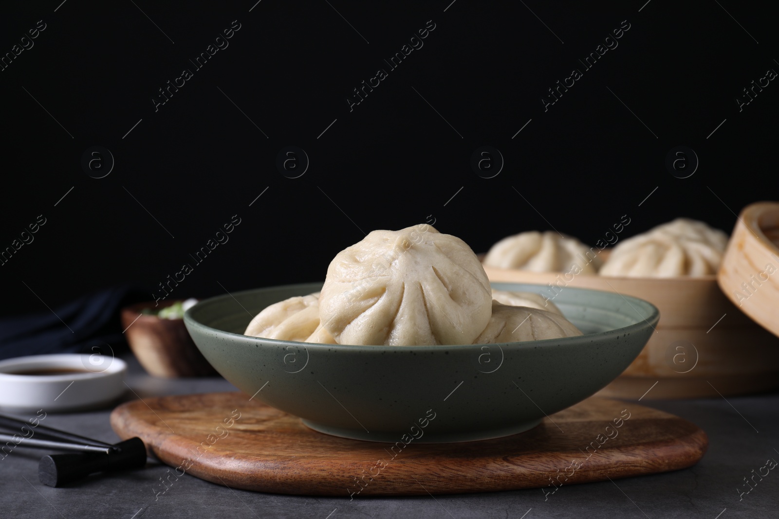 Photo of Delicious bao buns (baozi) in bowl on grey table, closeup