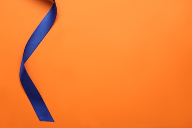Beautiful blue ribbon on orange background, top view. Space for text