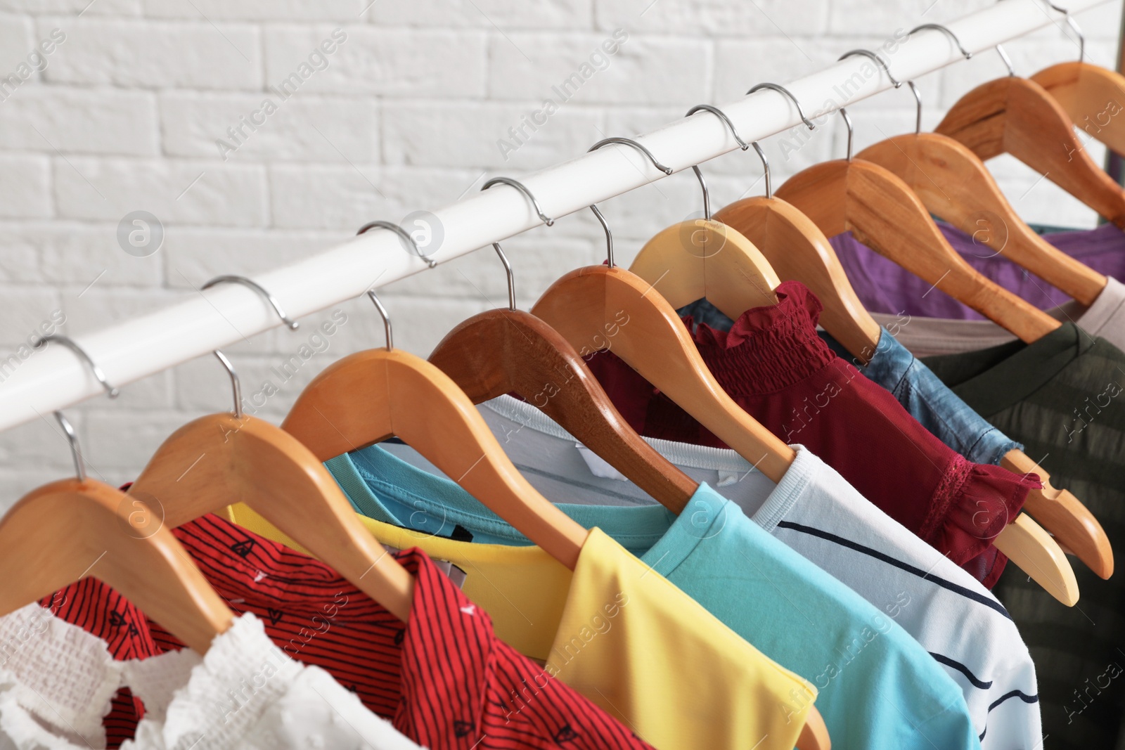 Photo of Wardrobe rack with stylish clothes near brick wall indoors, closeup