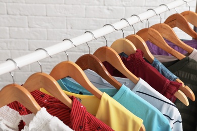 Wardrobe rack with stylish clothes near brick wall indoors, closeup