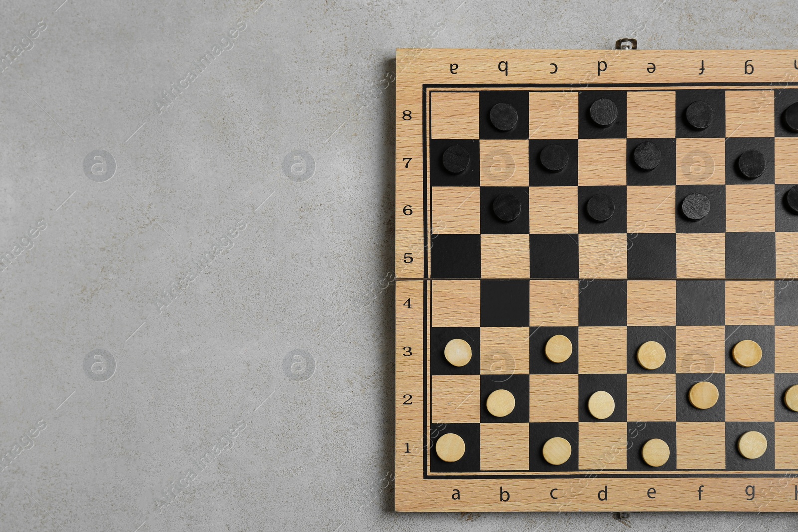 Photo of Wooden checkerboard with game pieces on light grey background, top view. Space for text