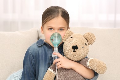 Sick little girl with toy bear using nebulizer for inhalation at home