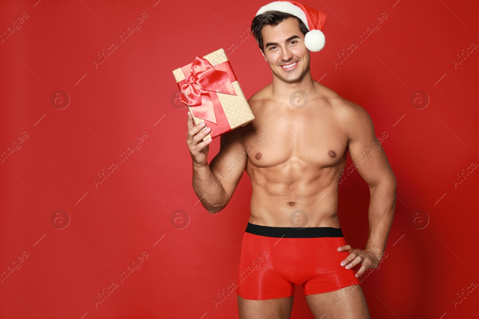 Photo of Sexy shirtless Santa Claus with gift on red background, space for text