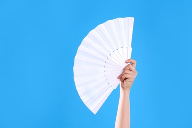 Woman holding white hand fan on light blue background, closeup