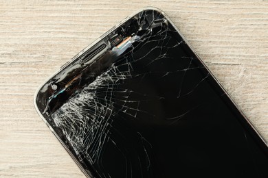 Photo of Top view of smartphone with cracked screen on light beige wooden background, closeup. Device repair