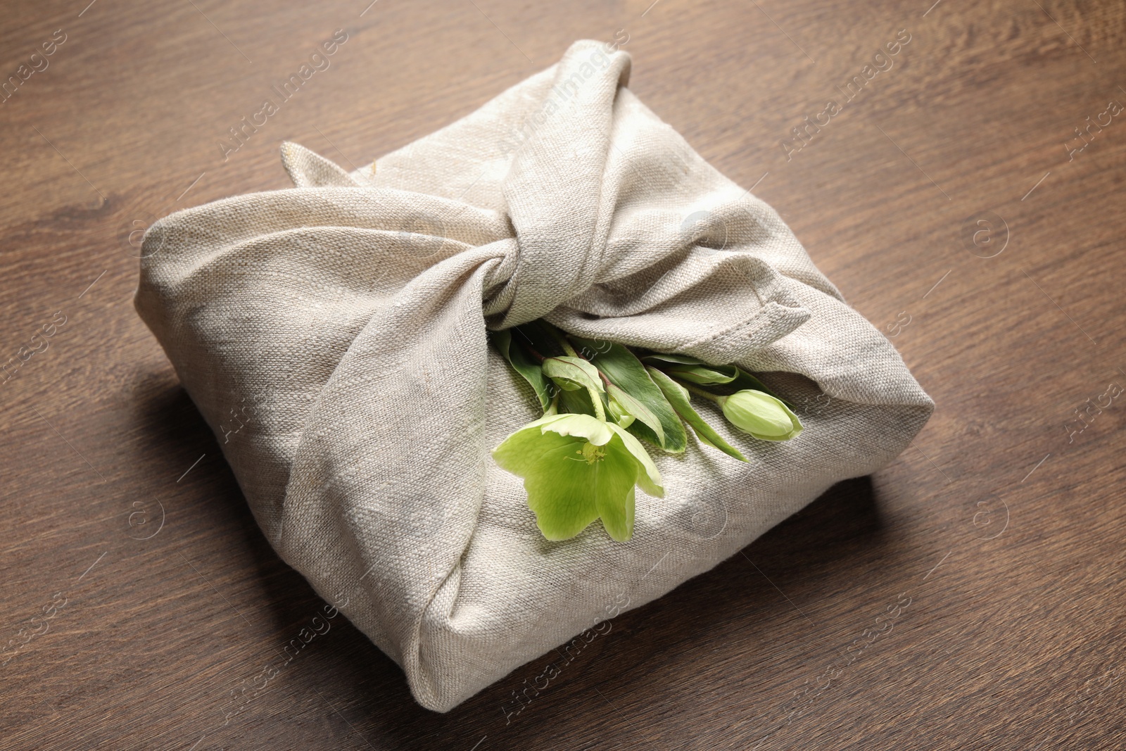 Photo of Furoshiki technique. Gift packed in white fabric decorated with beautiful flowers on wooden table