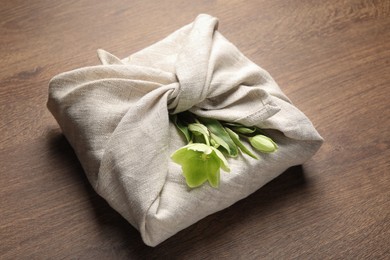 Photo of Furoshiki technique. Gift packed in white fabric decorated with beautiful flowers on wooden table