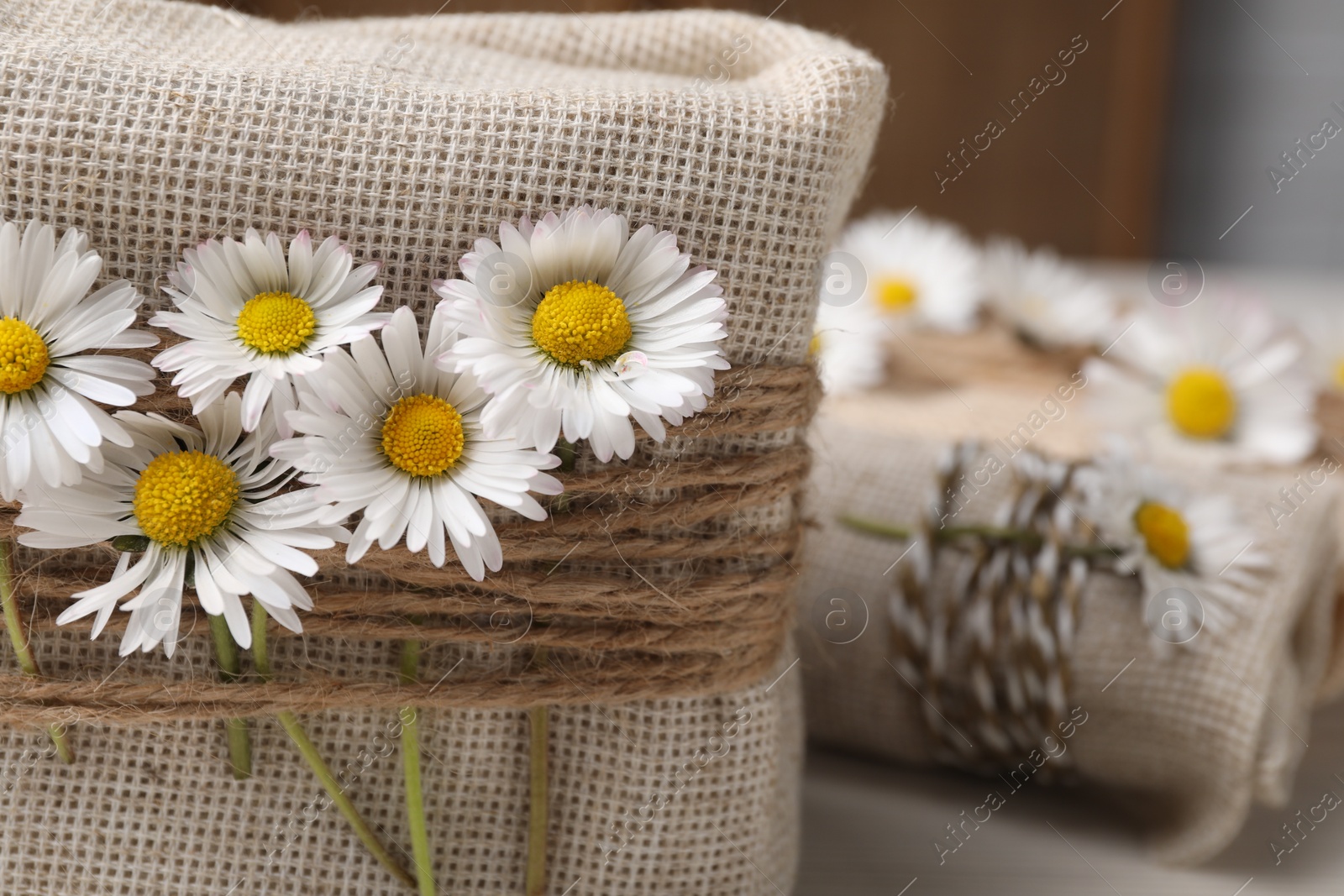 Photo of Gifts packed in burlap fabric, beautiful chamomiles, and ropes, closeup. Space for text