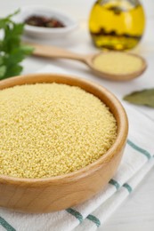 Bowl of raw couscous on white wooden table, closeup