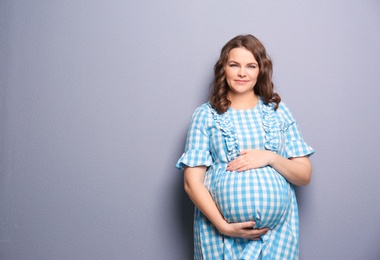 Photo of Young pregnant woman in casual clothes on grey background