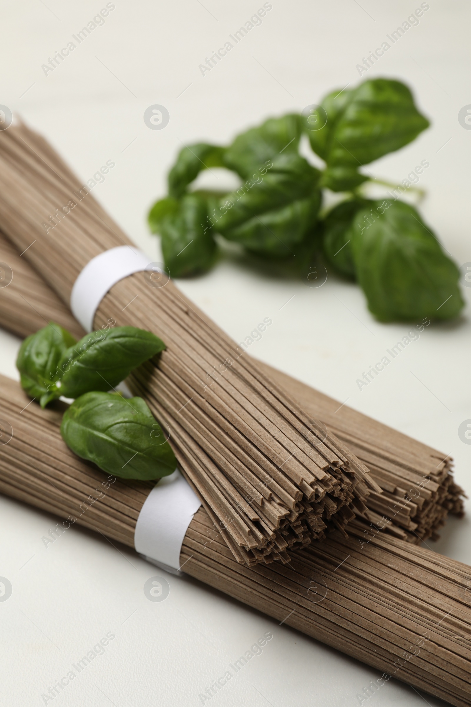 Photo of Uncooked buckwheat noodles (soba) and basil on white marble table, closeup