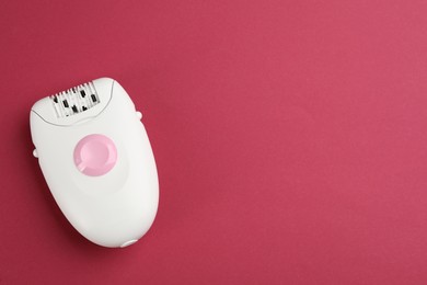 Modern epilator on crimson background, top view. Space for text