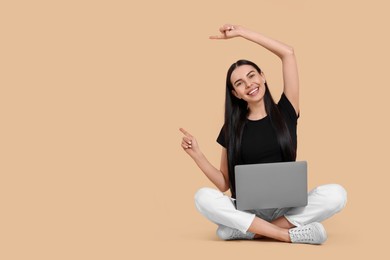 Photo of Happy woman with laptop pointing at something on beige background