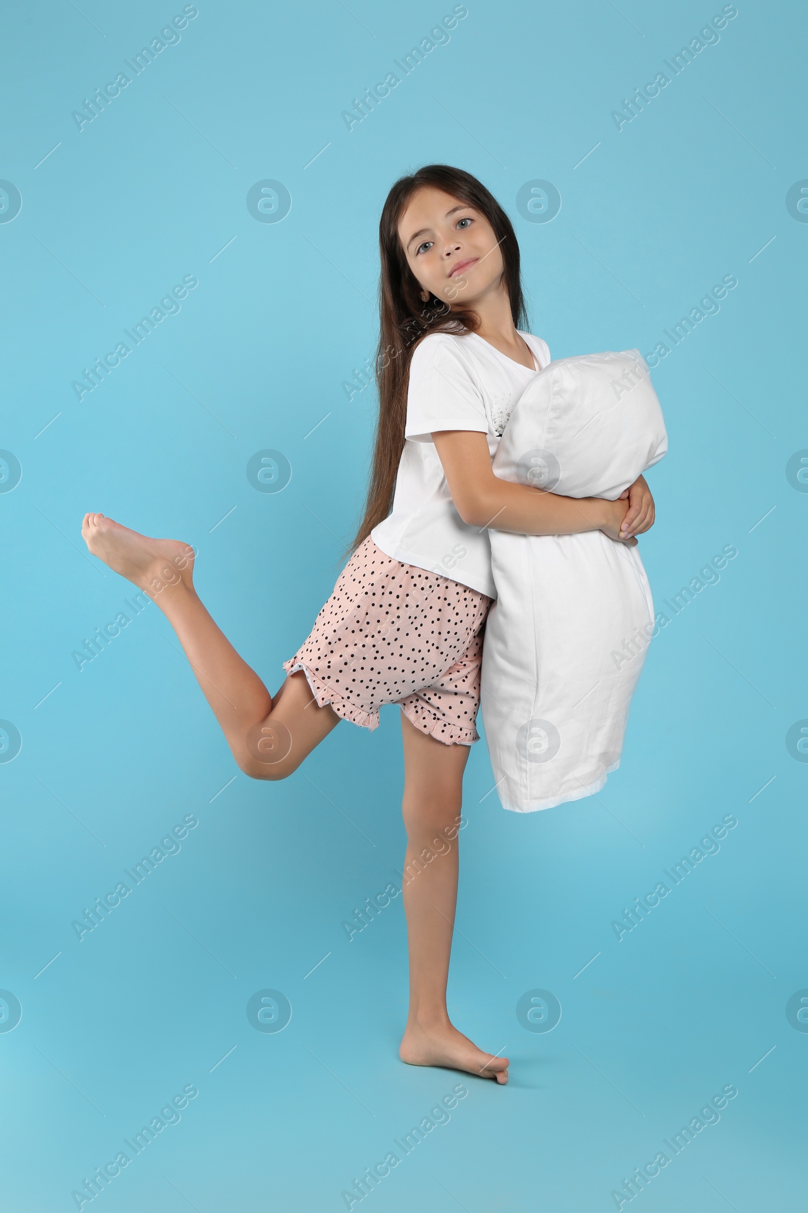 Photo of Cute girl wearing pajamas with pillow on light blue background