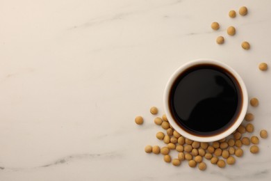 Soy sauce in bowl and soybeans on white marble table, flat lay. Space for text