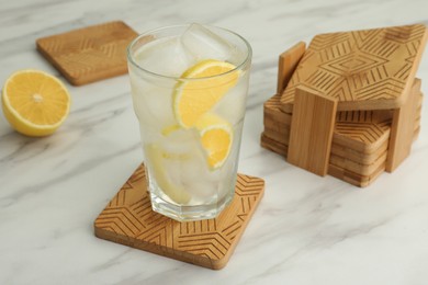 Photo of Glass of cocktail and stylish wooden cup coasters on white table