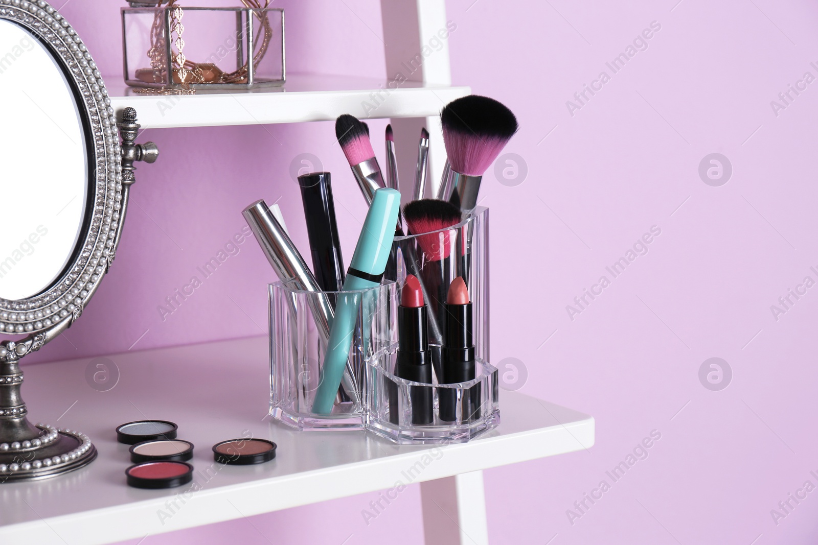 Photo of Organizer with cosmetic products for makeup on shelf near color wall