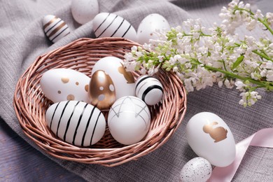 Many painted Easter eggs, branch with lilac flowers and ribbon on table